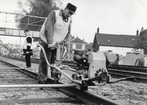 169012 Afbeelding van een wegwerker van de N.S. met een dwarsliggerboormachine tijdens werkzaamheden aan de spoorlijn ...